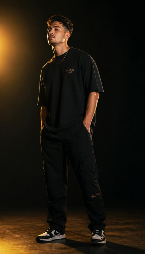 Modelo vestindo camiseta oversized preta GOTT com calça cargo, em estúdio com fundo escuro e luz dourada